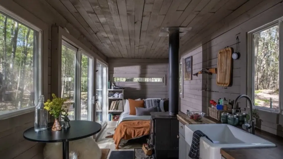 Warm off-grid tiny home interior with wood stove and forest views — The Foothills Tiny Home Company